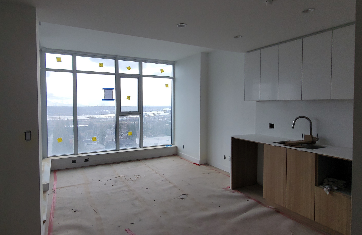 A kitchen under renovation, with newly installed windows, and floor installation in progress.