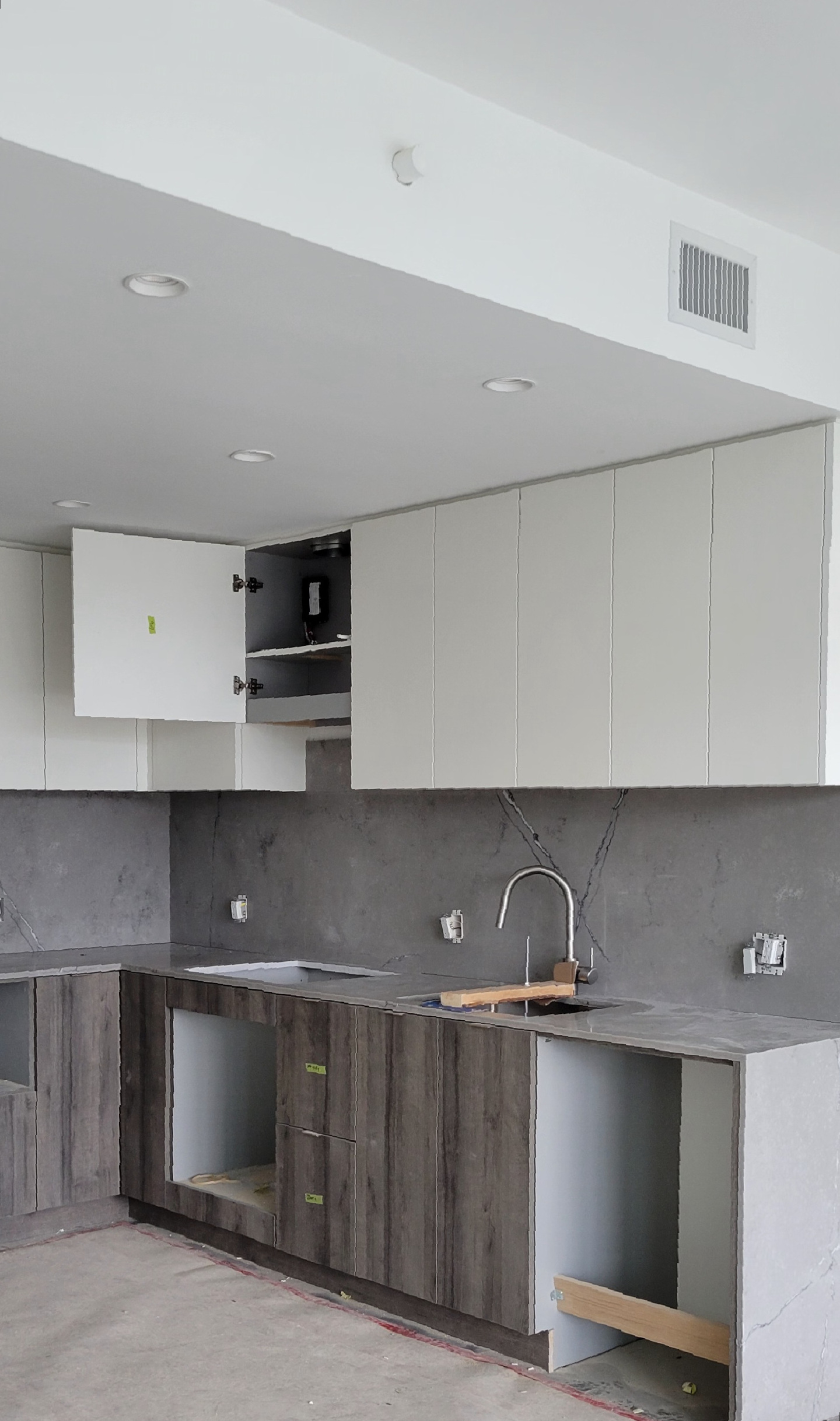 A renovated kitchen with new shiny upper cabinets, wooden lower cabinets, and marbel wall tiles.