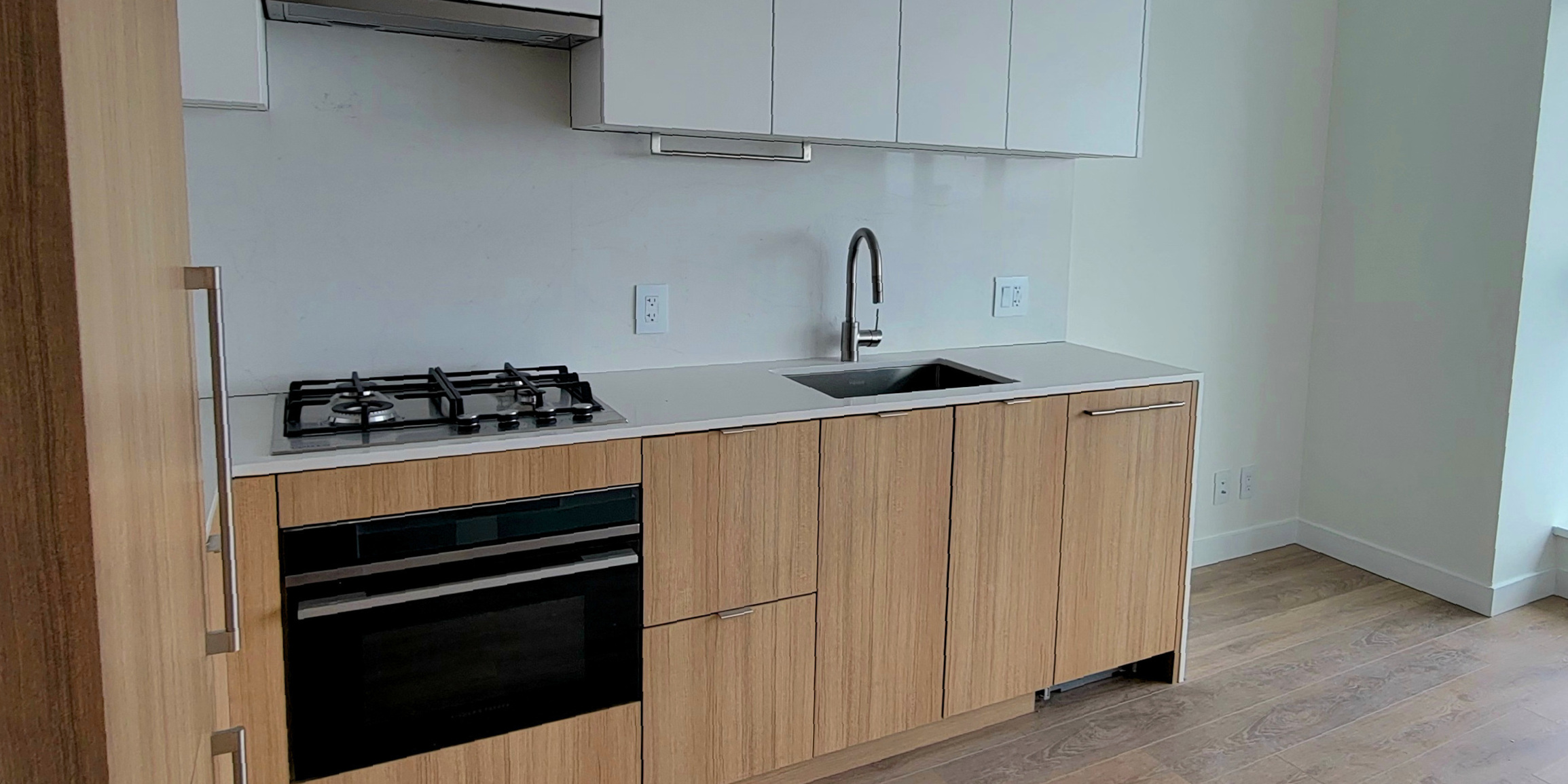 Completed kitchen renovation, with installed cabinets, hardwood flooring, and wall tiles.
