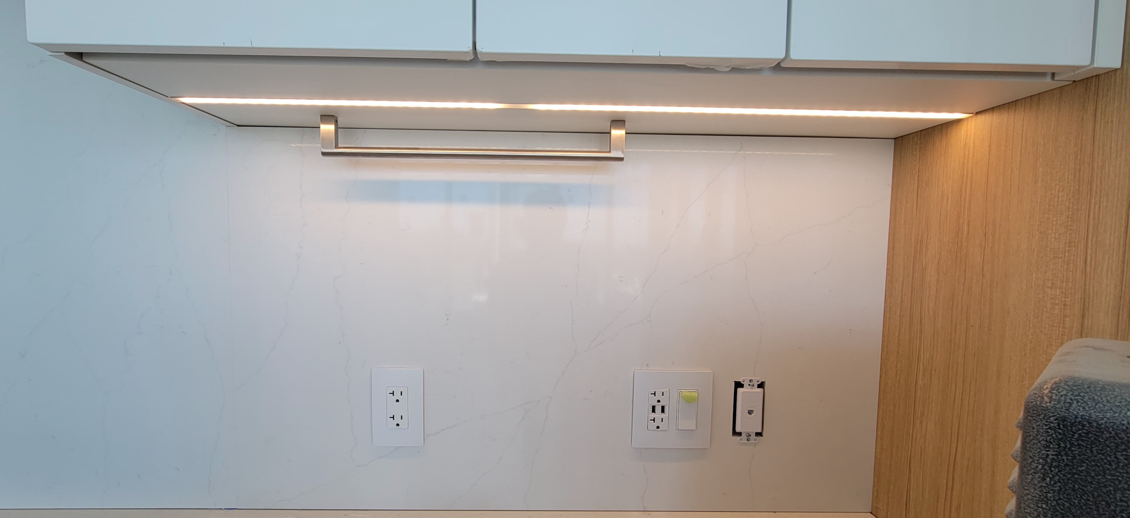 A closeup of installed marbel kitchen tiles and under-counter lights.