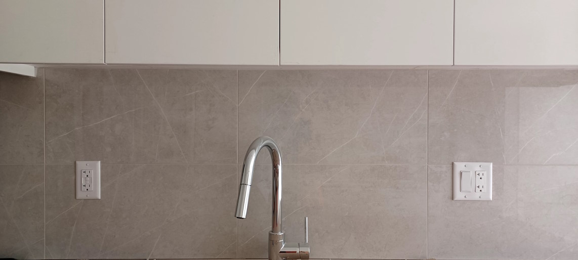 Installed kitchen wall tiles, behind a shiny chrome tap.