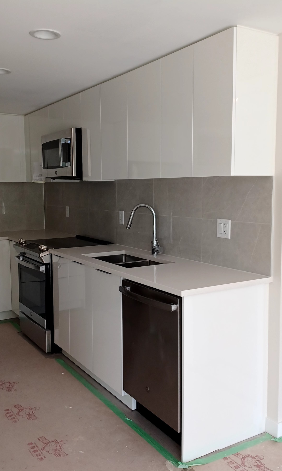 A newly-renovated kitchen, with a modern design and shiny new cabinets, wall tiles, and painted ceiling.