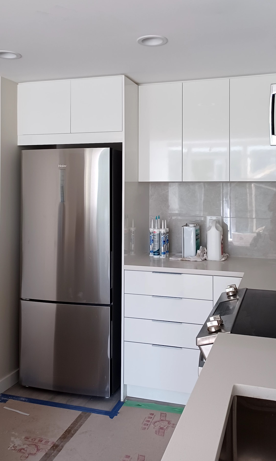 A newly-renovated kitchen, with a modern design and shiny new cabinets, wall tiles, painted ceiling, and a new refrigerator.