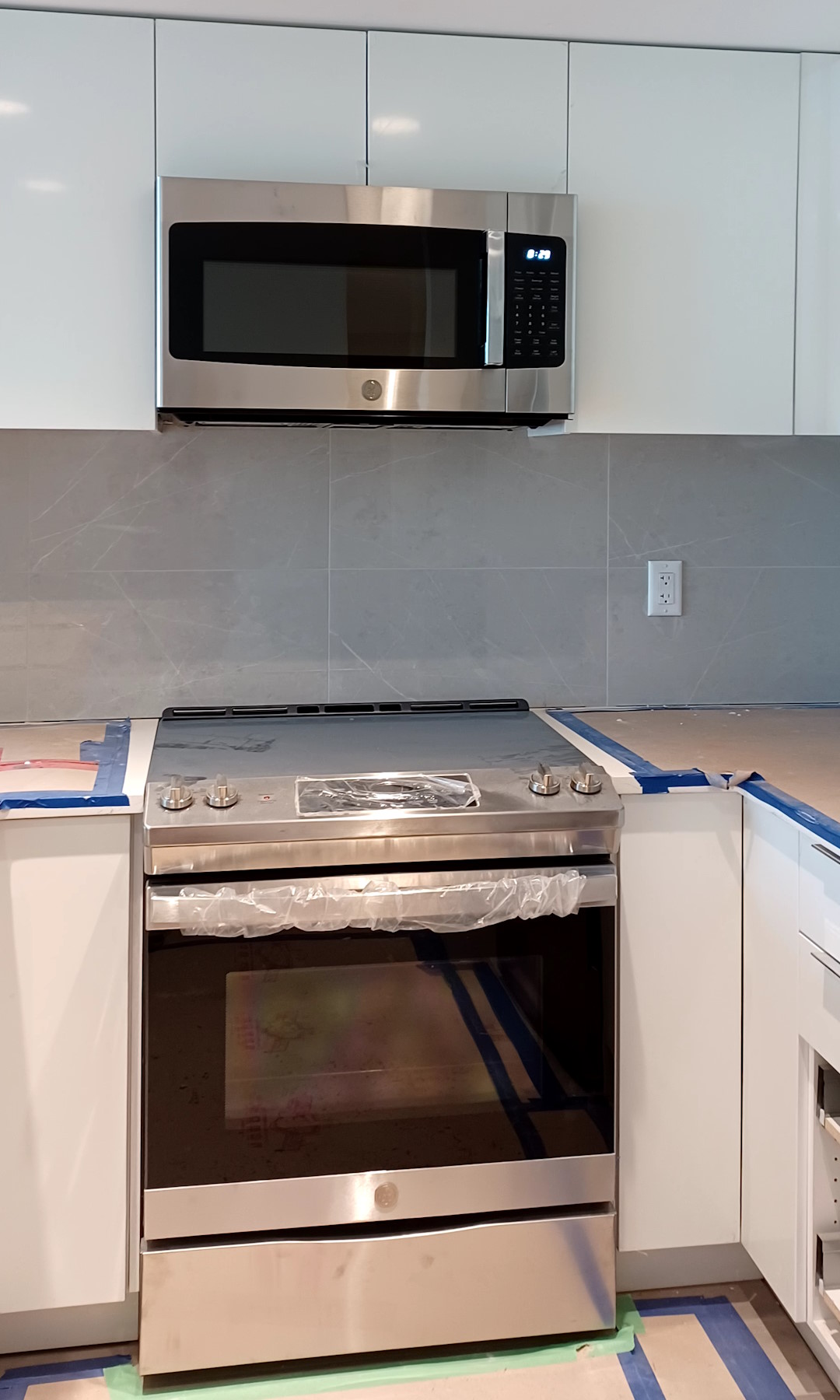A newly-renovated kitchen, with a modern design and shiny new cabinets, wall tiles, and painted ceiling, and new oven and microwave.