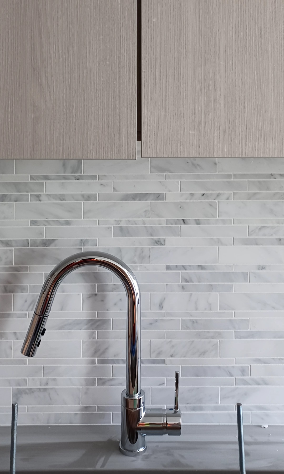 Shinny chrome kitchen tap, with an installed wooden kitchen cabinet above it and a bright new tiled wall.